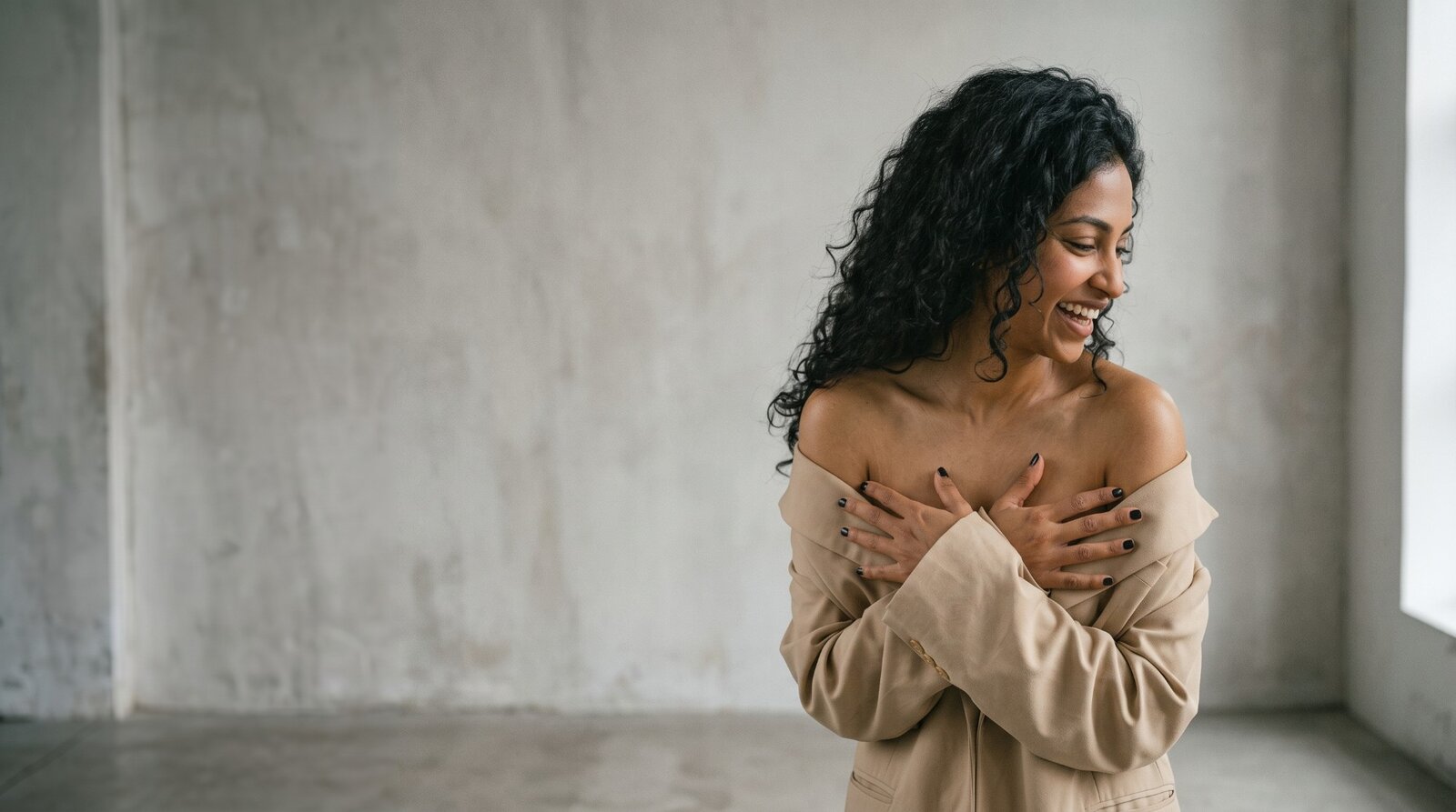 A smiling, confident woman wrapped in a blazer with her arms crossed over her chest.